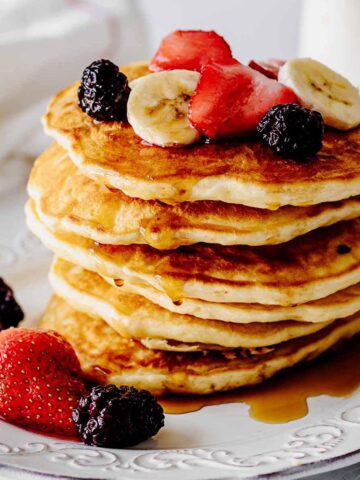Stack of homemade pancakes topped with berries and sliced bananas on a white plate
