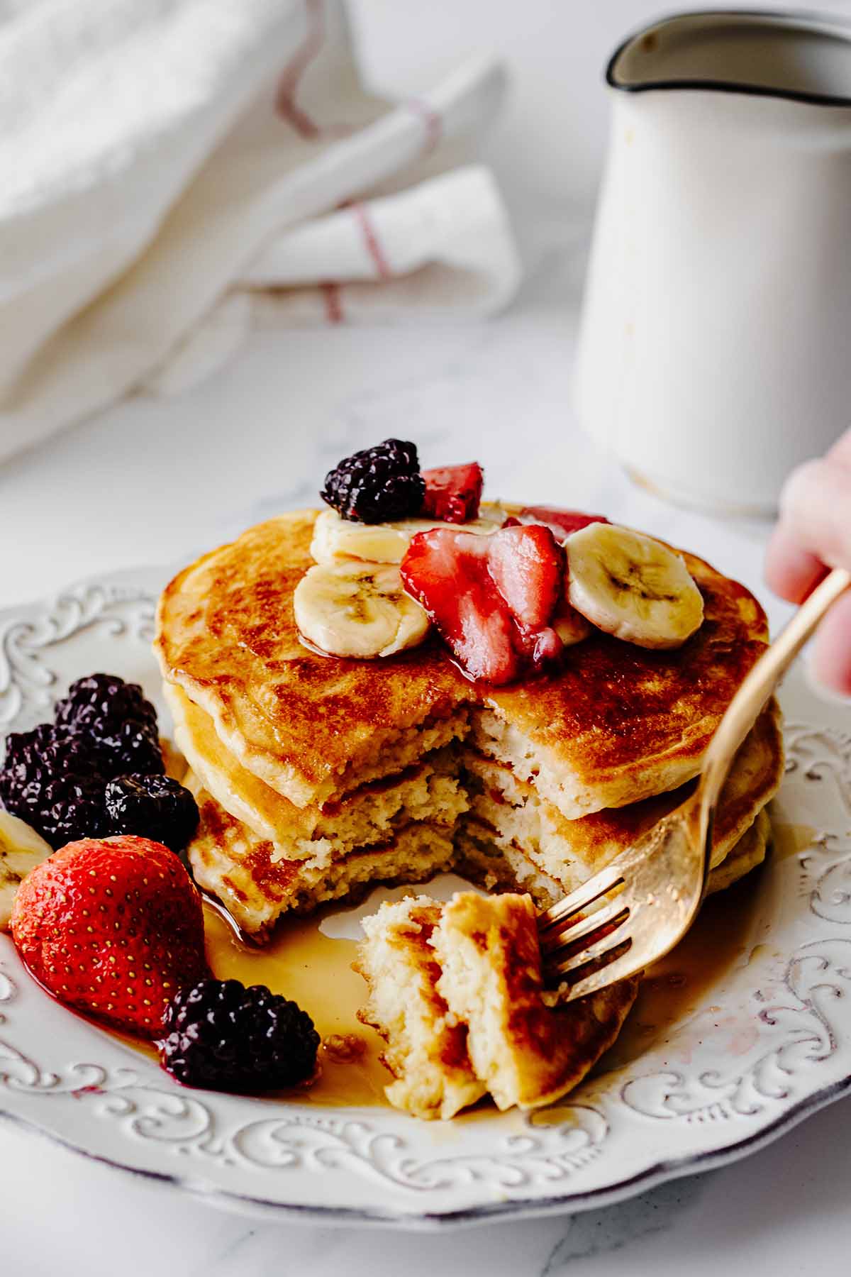 Short stack of pancakes topped with berries and sliced bananas with a bite on a fork ready to be eaten