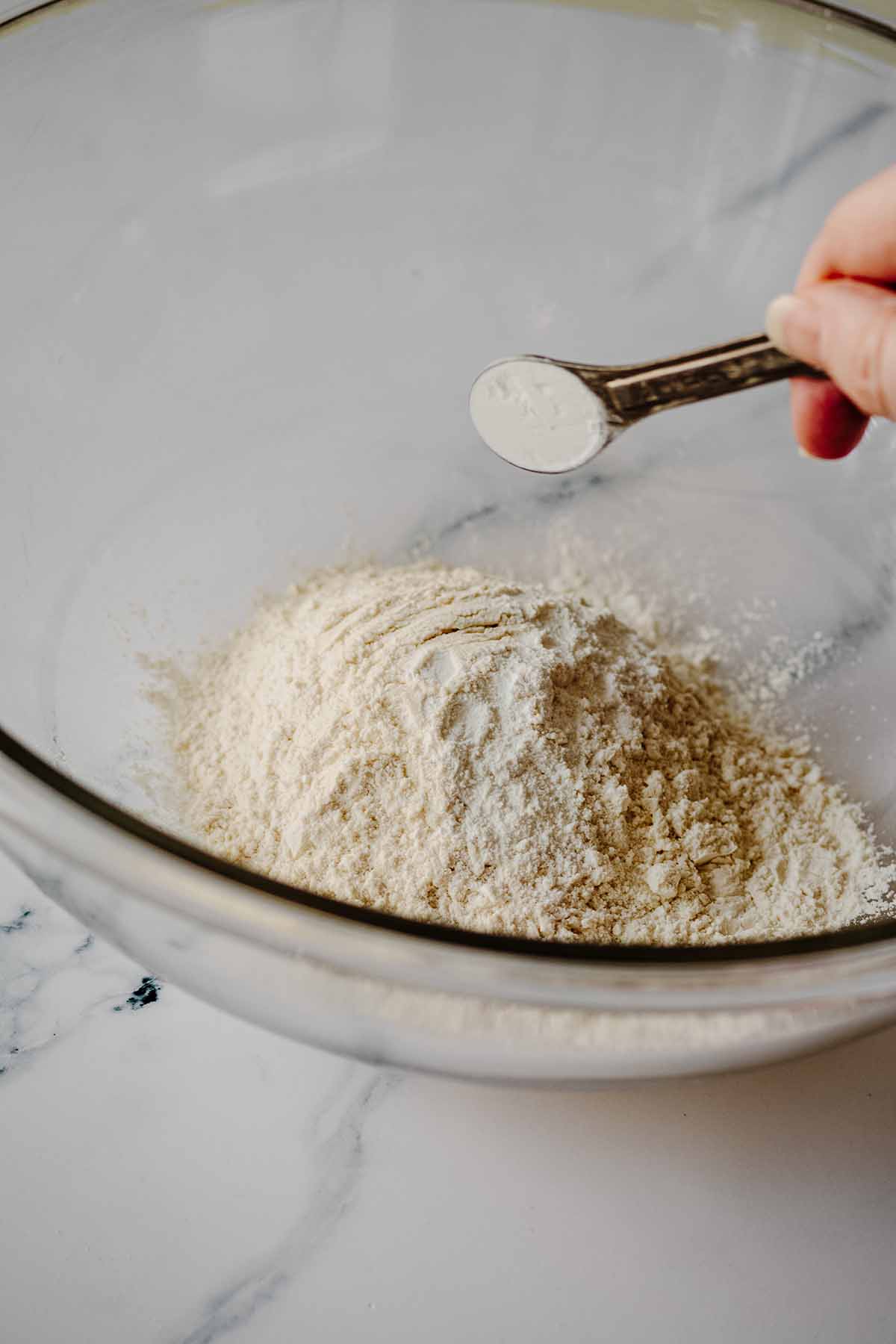 Baking powder being added to flour in a glass bowl