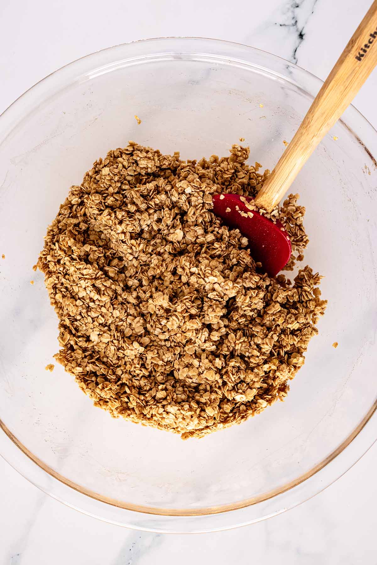 Overhead view of oat mixture in a glass bowl with a red spatula