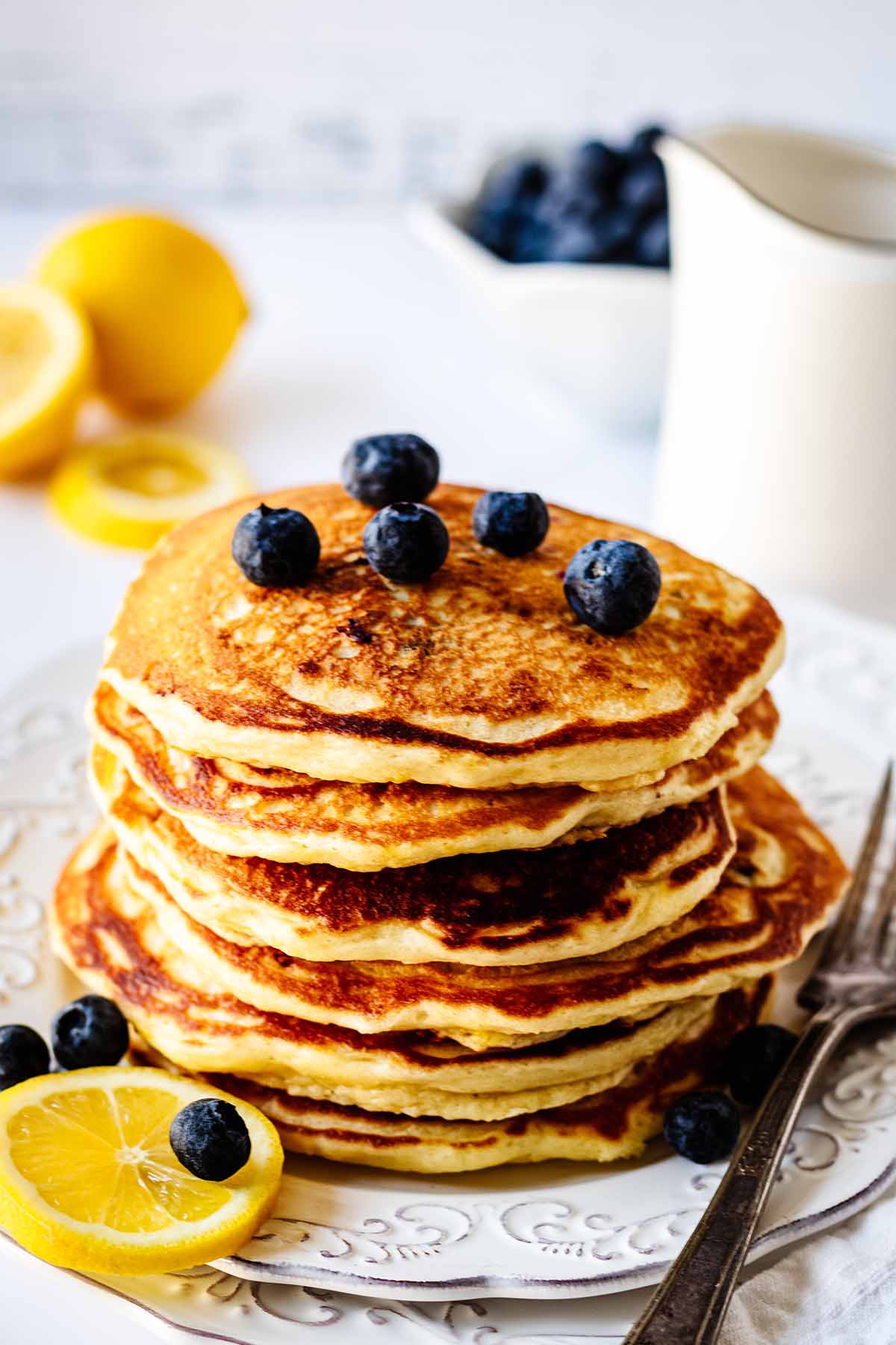 Stack of blueberry pancakes topped with blueberries on a white plate