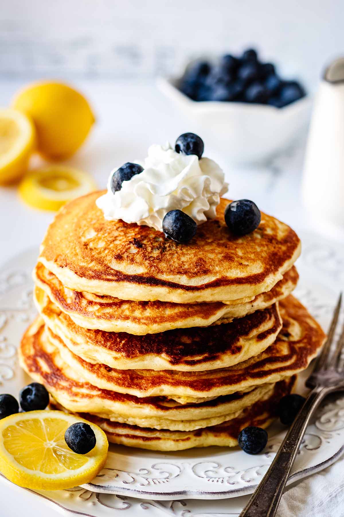 Stack of lemon blueberry pancakes topped with whipped cream and blueberries on a white plate