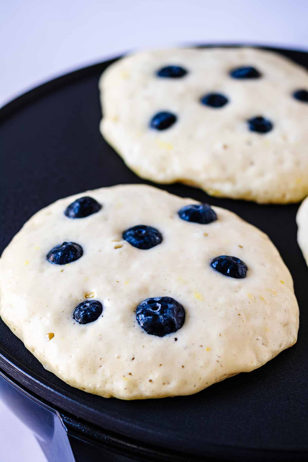 Pancakes topped with blueberries cooking on a griddle