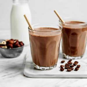 Mocha shake in two glass glasses with straws and coffee beans on a white marble counter