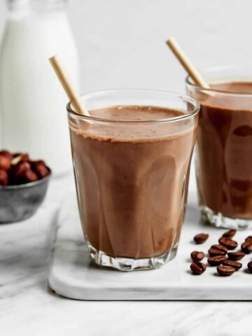 Mocha shake in two glass glasses with straws and coffee beans on a white marble counter