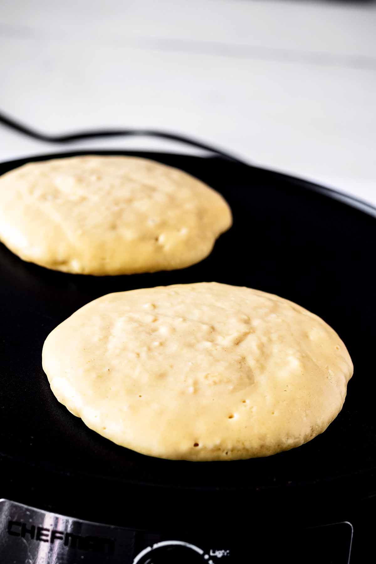 Two pancakes cooking on a griddle