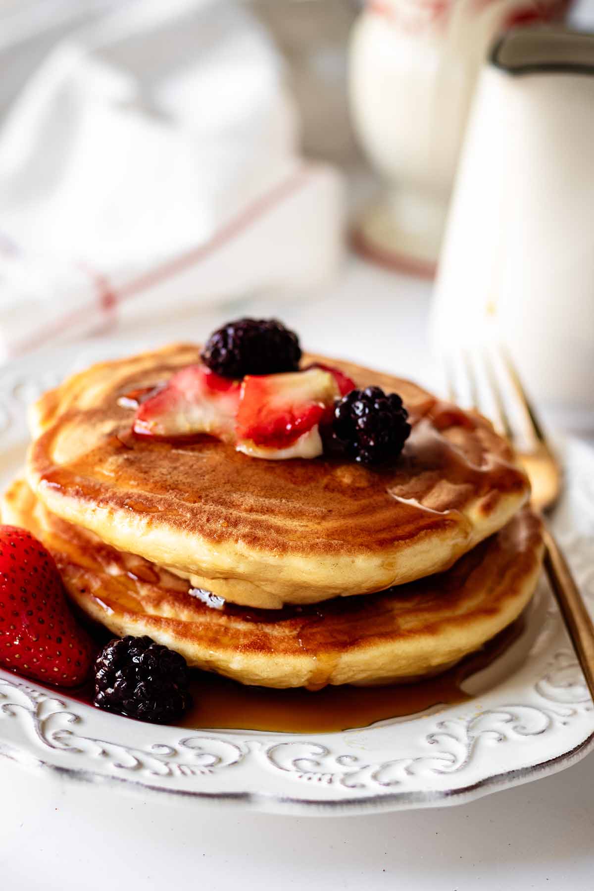 Short stack of pancakes topped with berries and syrup on a white plate