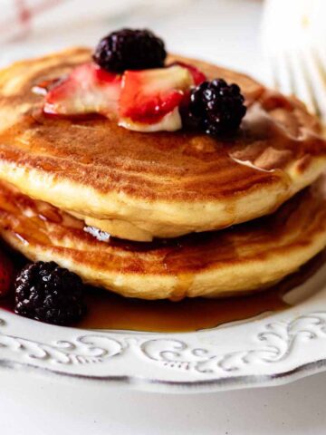 Short stack of pancakes topped with berries and syrup on a white plate