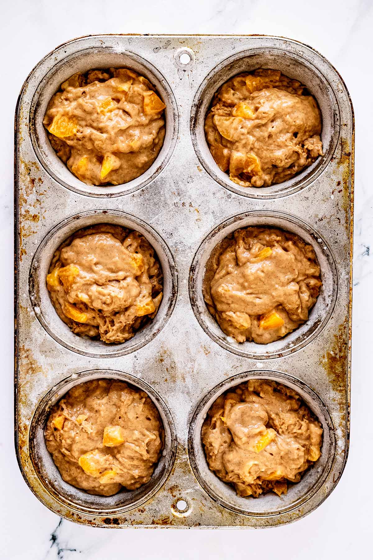 Overhead view of peach muffin batter in a muffin tin