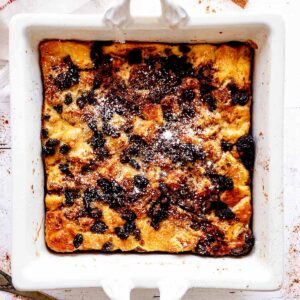 Overhead view of raisin bread pudding in a white baking dish with powdered sugar sprinkled over the top