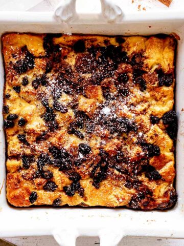 Overhead view of raisin bread pudding in a white baking dish with powdered sugar sprinkled over the top