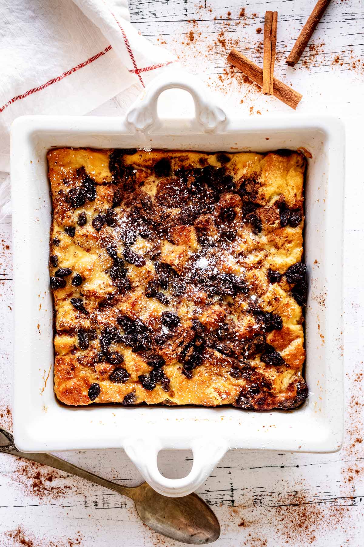 Overhead view of raisin bread pudding in a white baking dish with powdered sugar sprinkled over the top