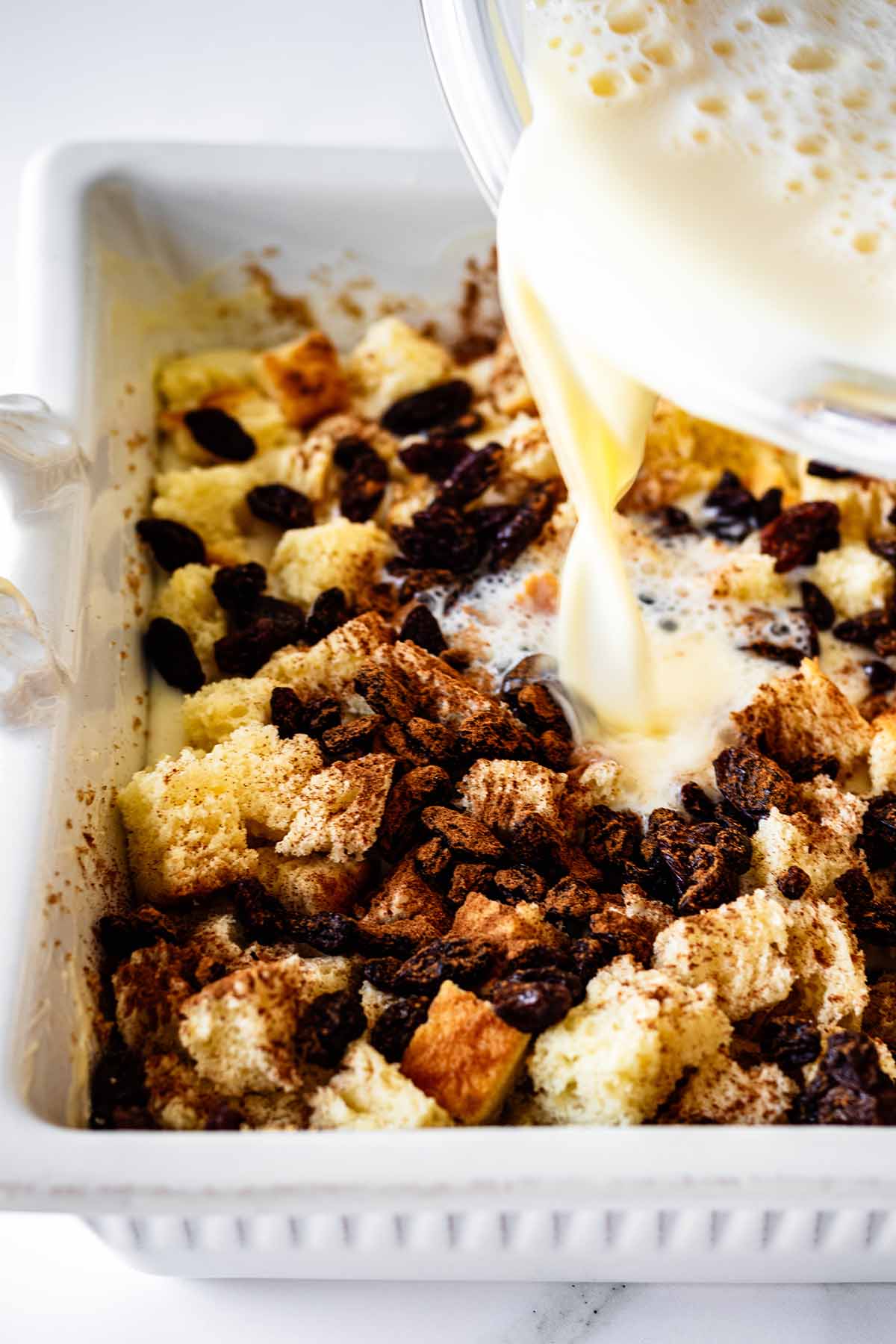 Wet ingredients being poured over the top of diced bread and raisins