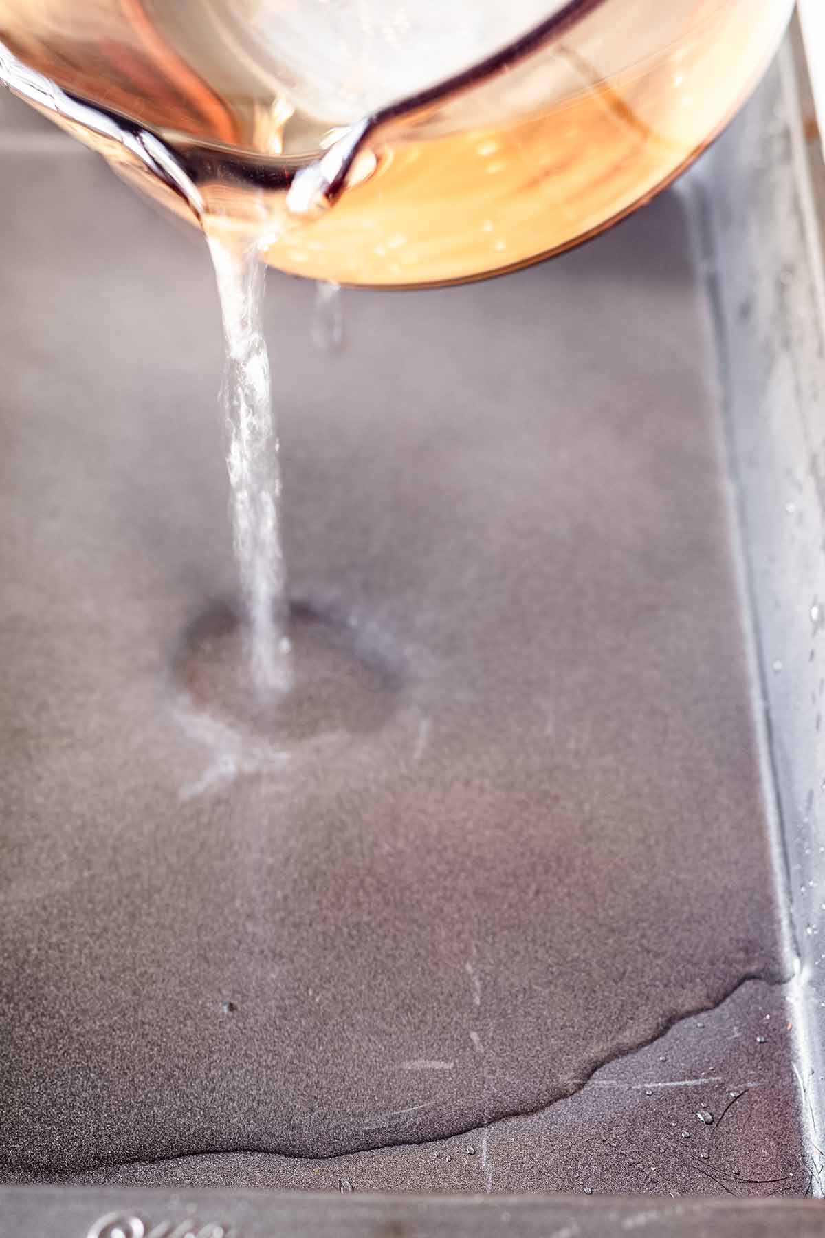 Hot water being poured into a large metal baking dish