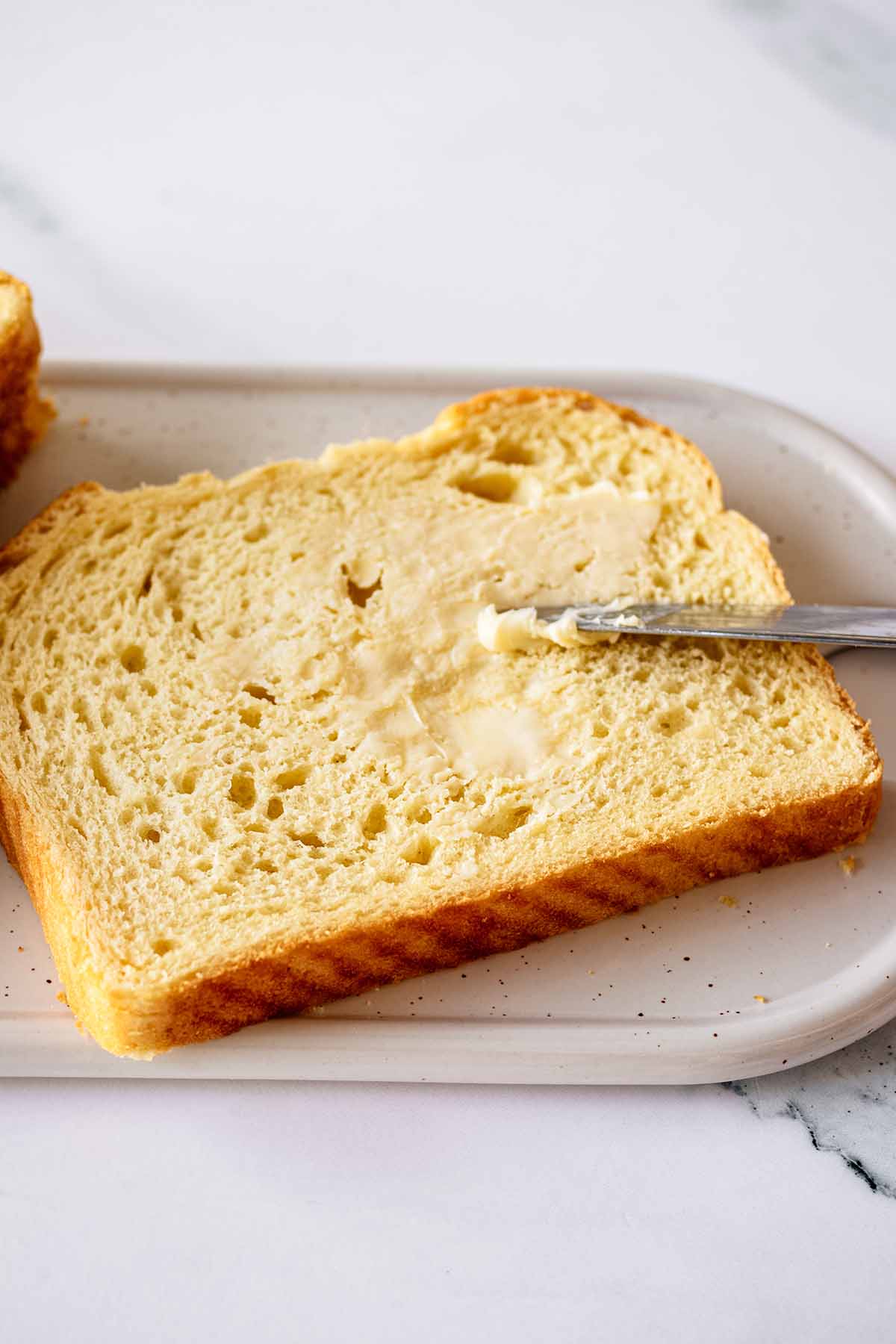 Slice of bread being buttered on a white platter