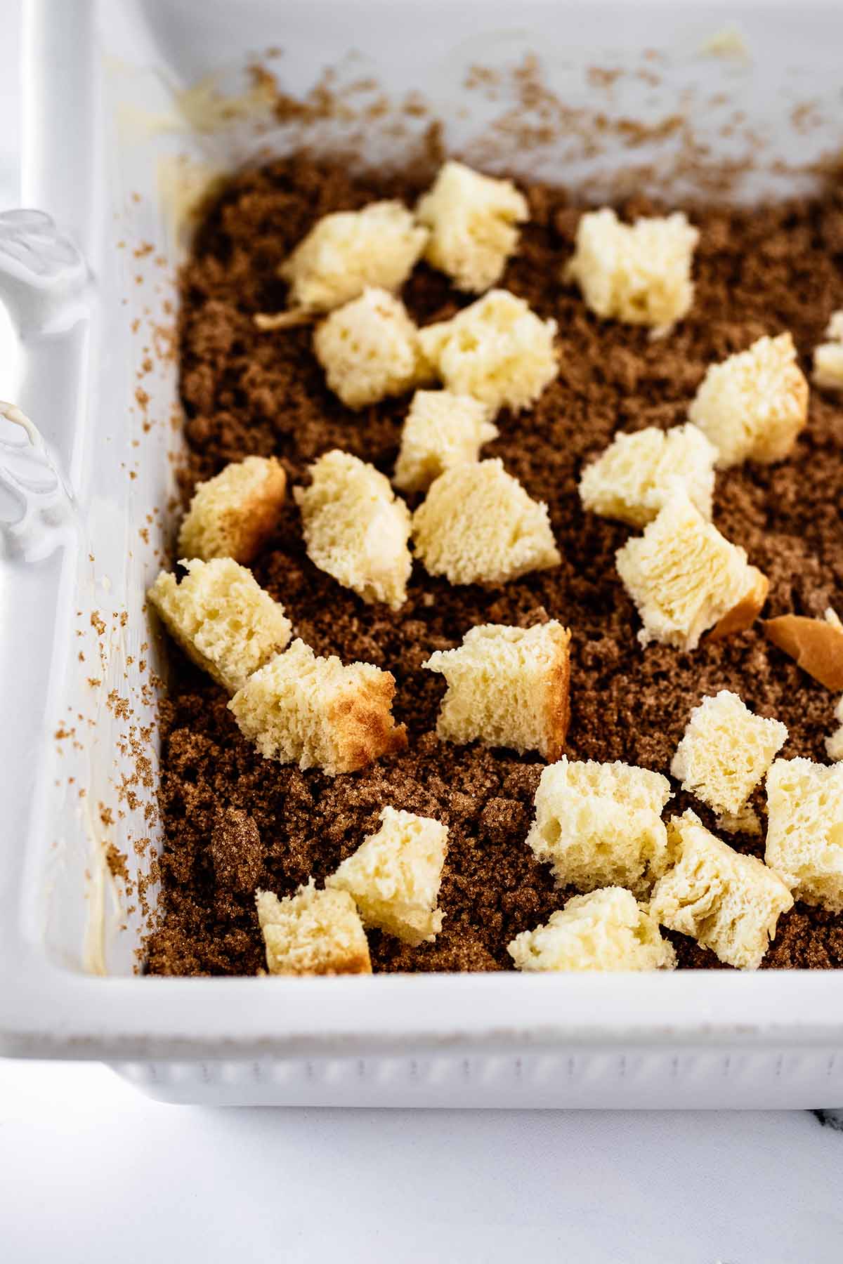 Diced bread sprinkled on top of brown sugar in a white baking dish