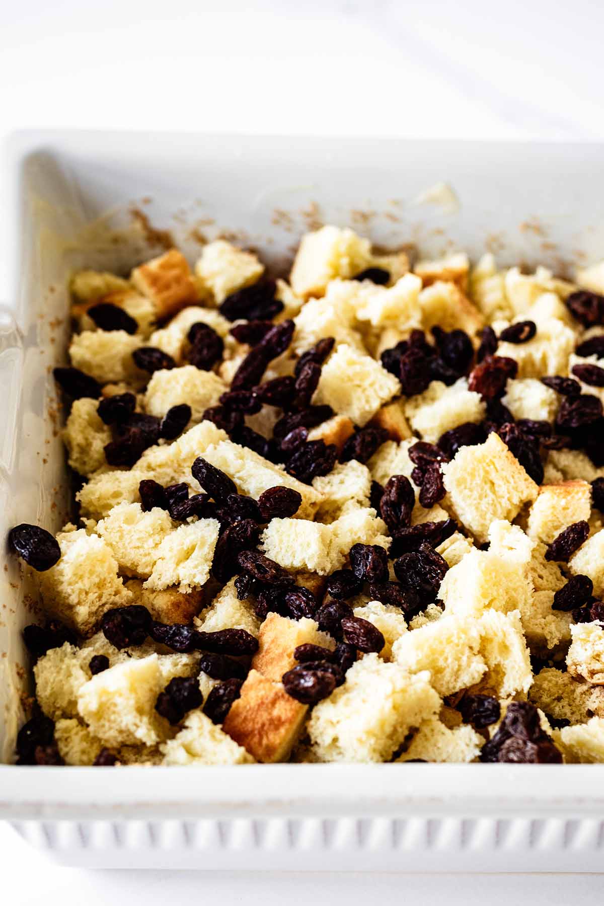 Raisins sprinkled on top of diced bread in baking dish