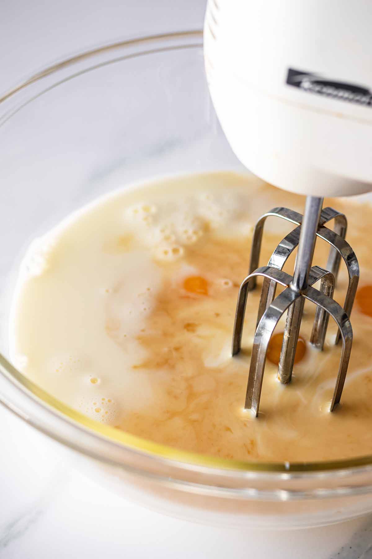 Wet ingredients in a glass bowl with an electric mixer