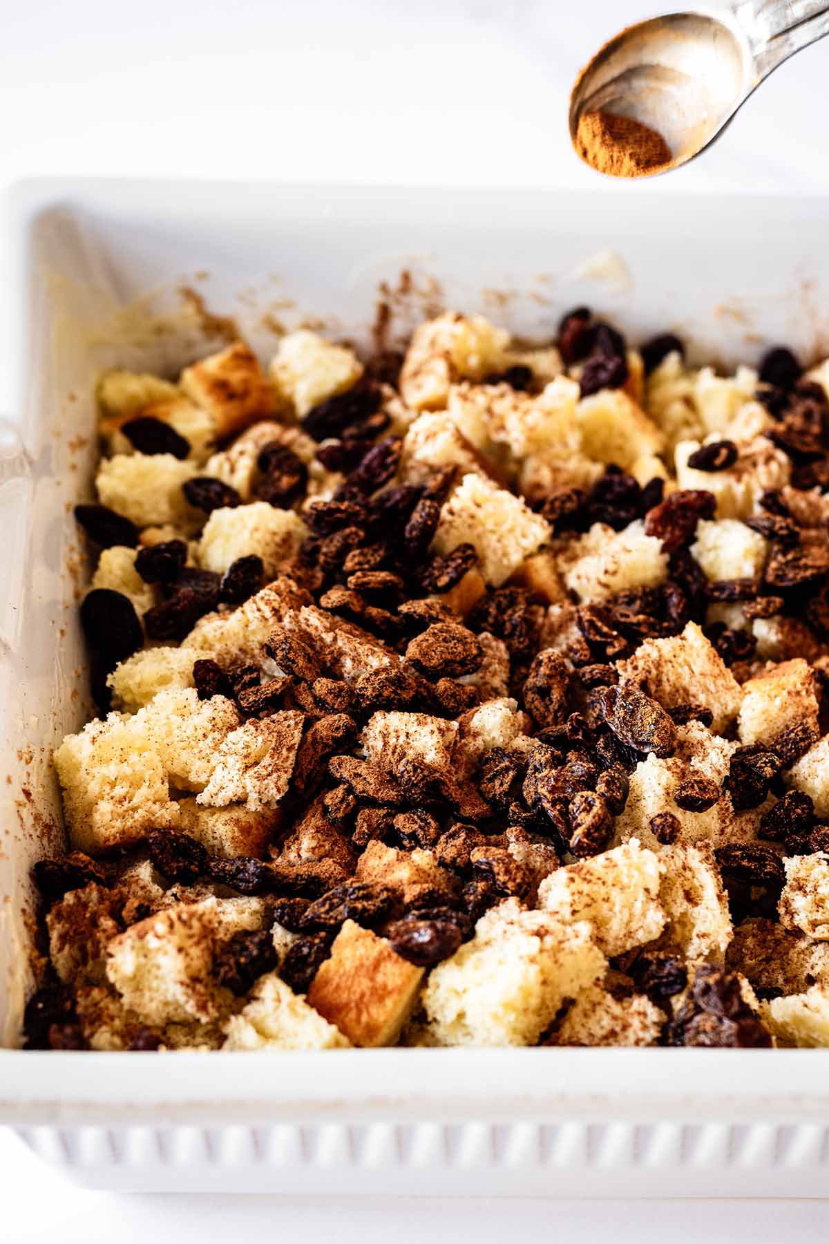 Cinnamon being sprinkled on top of diced bread and raisins