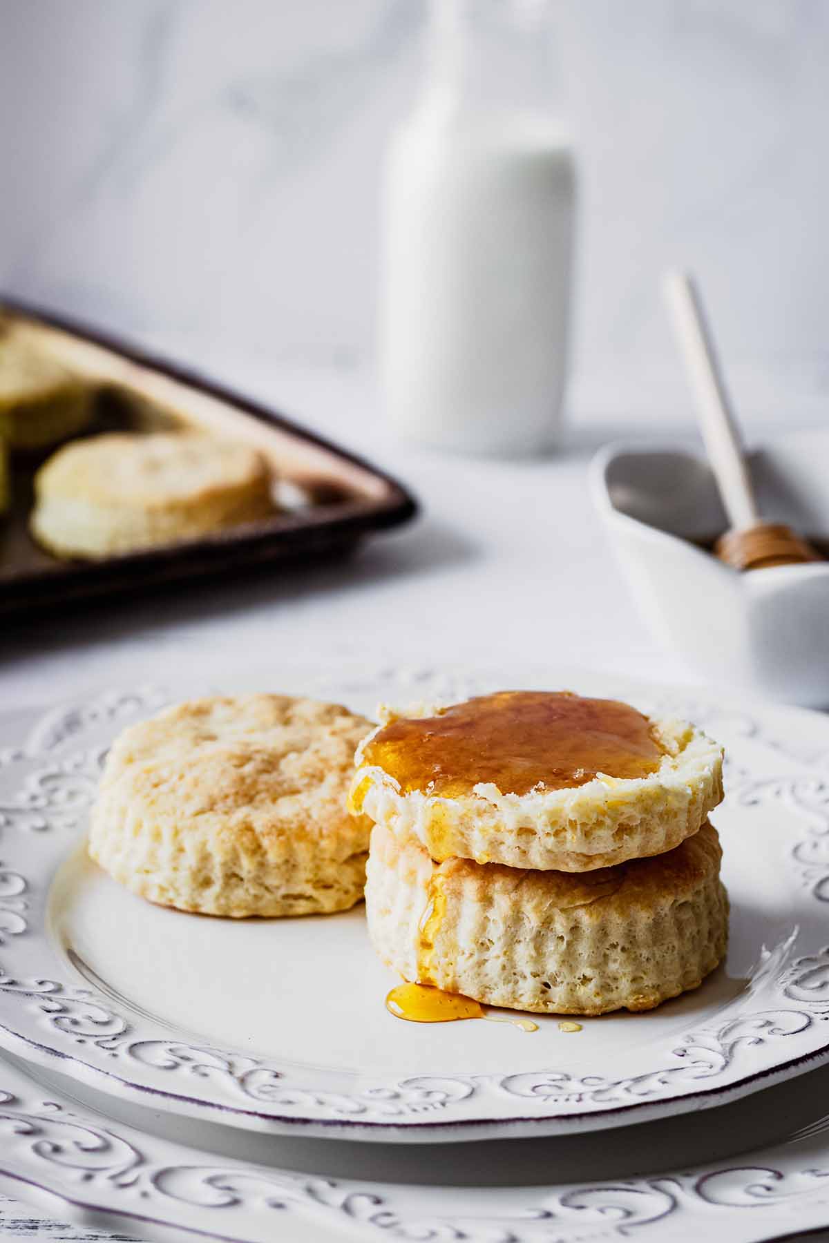 Stack of biscuits topped with honey on a white plate