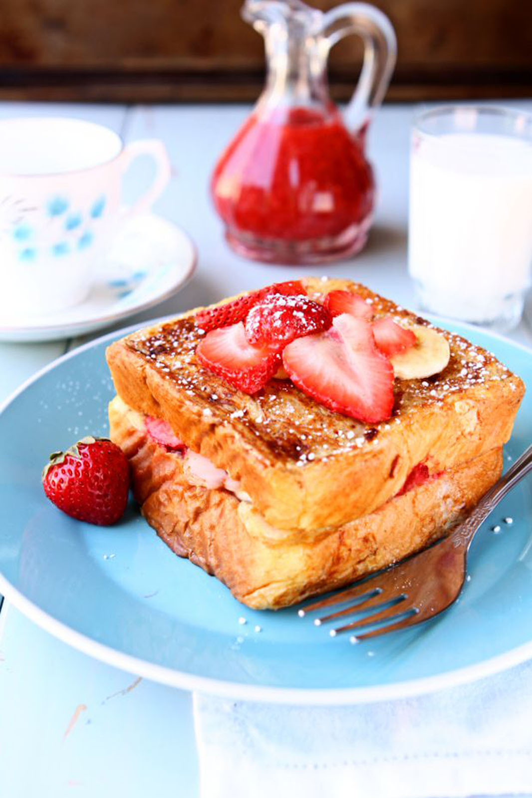 French toast on a blue plate with a carafe of strawberry compote in the background