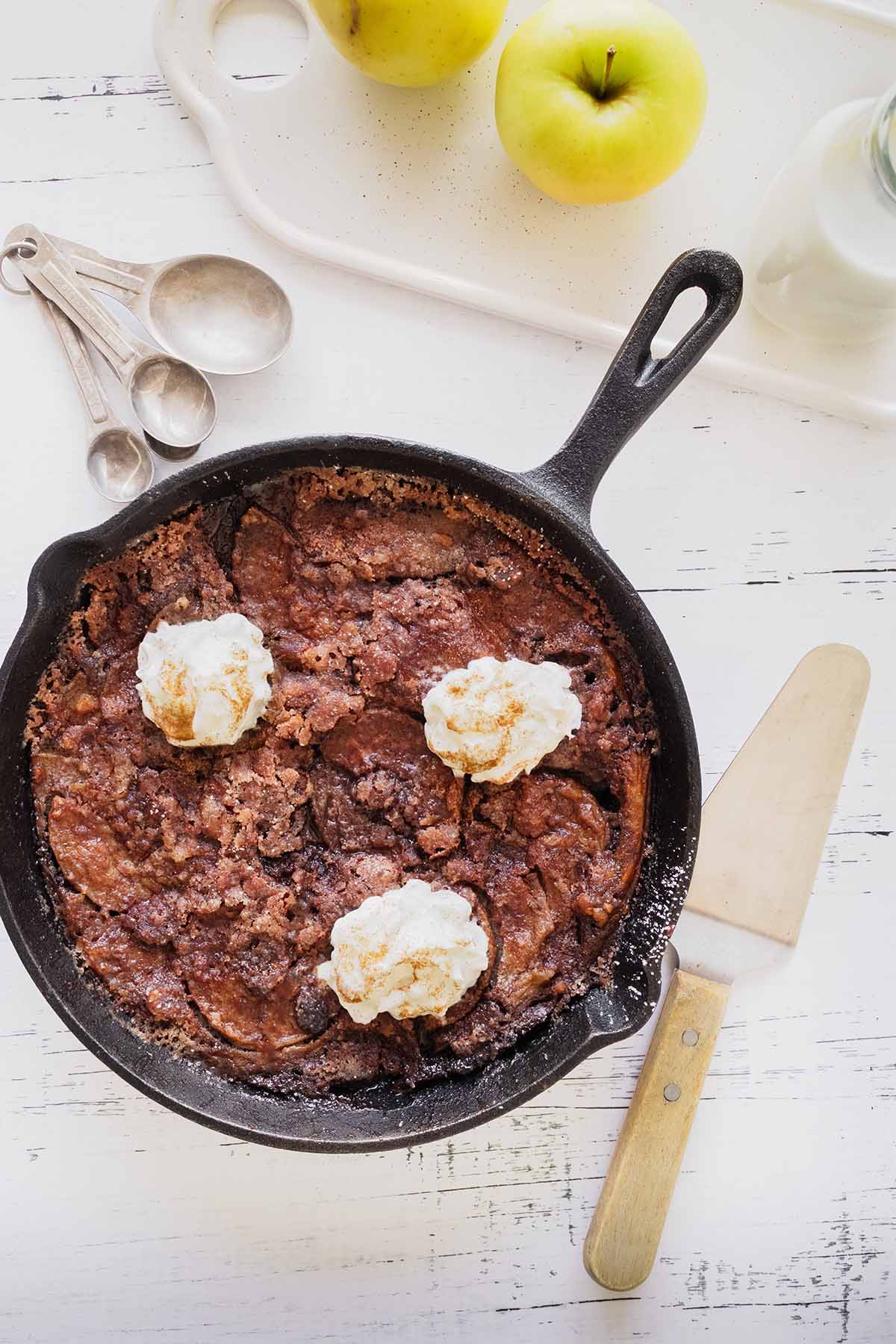 Overhead close up of apple breakfast bake topped with whipped cream in a cast iron skillet