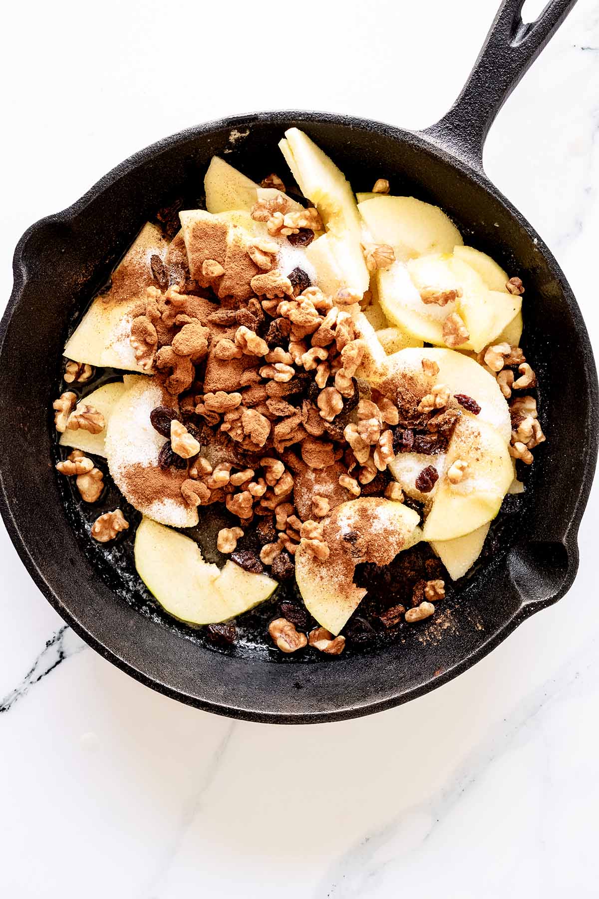 Overhead view of apples, walnuts, raisins, cinnamon and sugar in a cast iron skillet