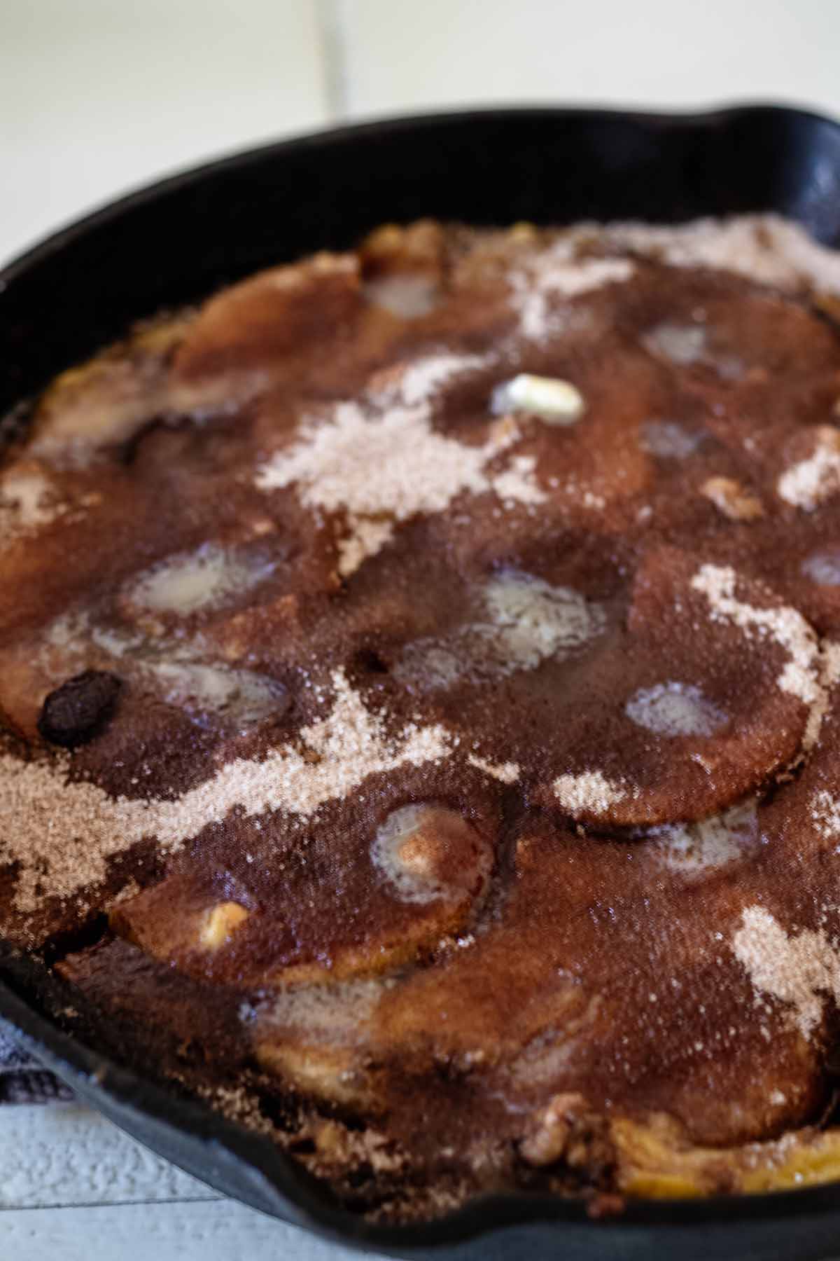 Cinnamon sugar and butter sprinked on top of batter and apple mixture in a cast iron skillet