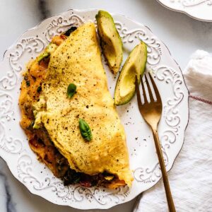 Close up overhead view of keto omelette on a white plate with a gold fork and avocado slices