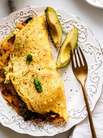 Close up overhead view of keto omelette on a white plate with a gold fork and avocado slices