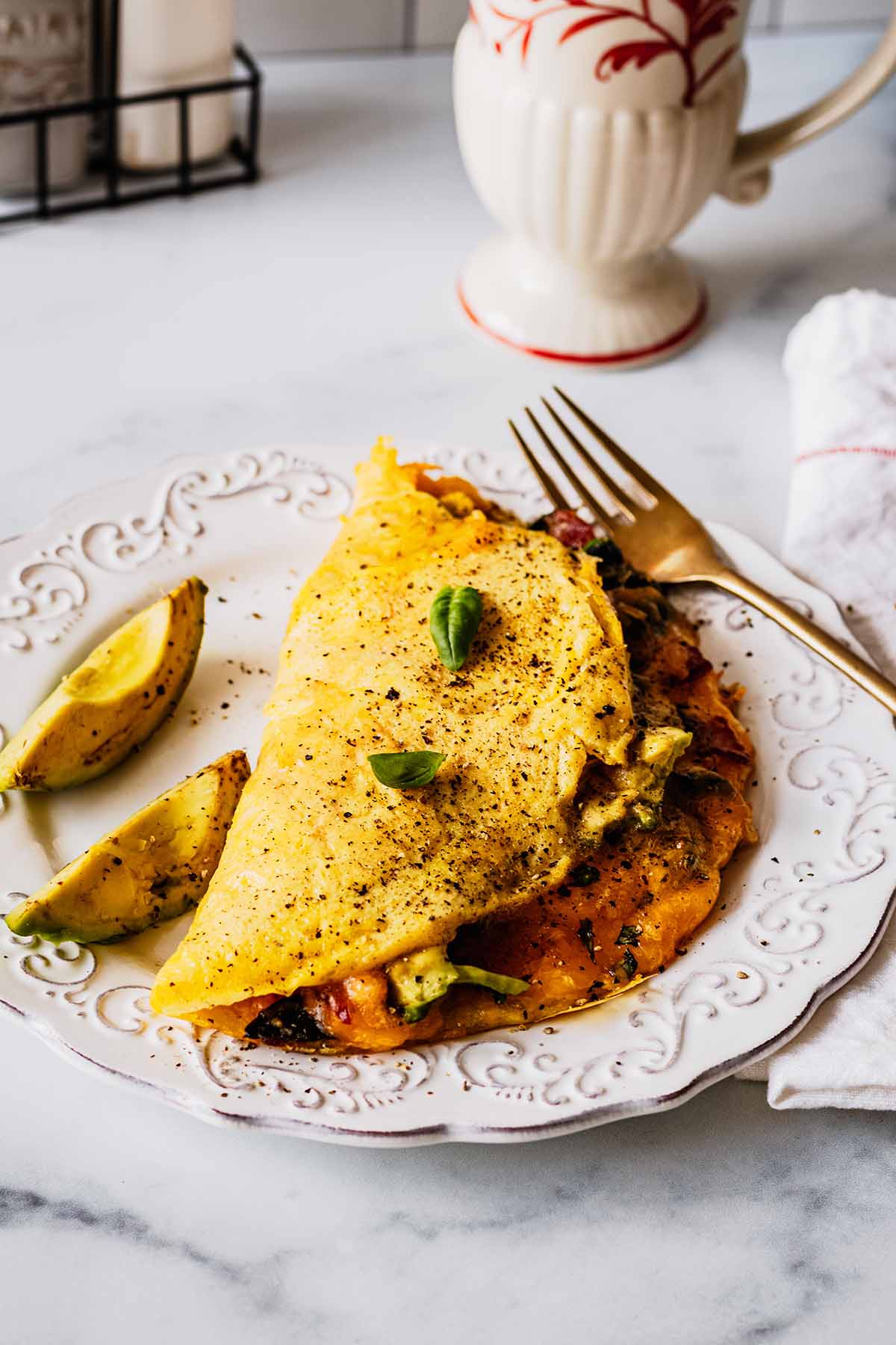 Front view of keto omelette on a white plate with avocado slices and a gold fork