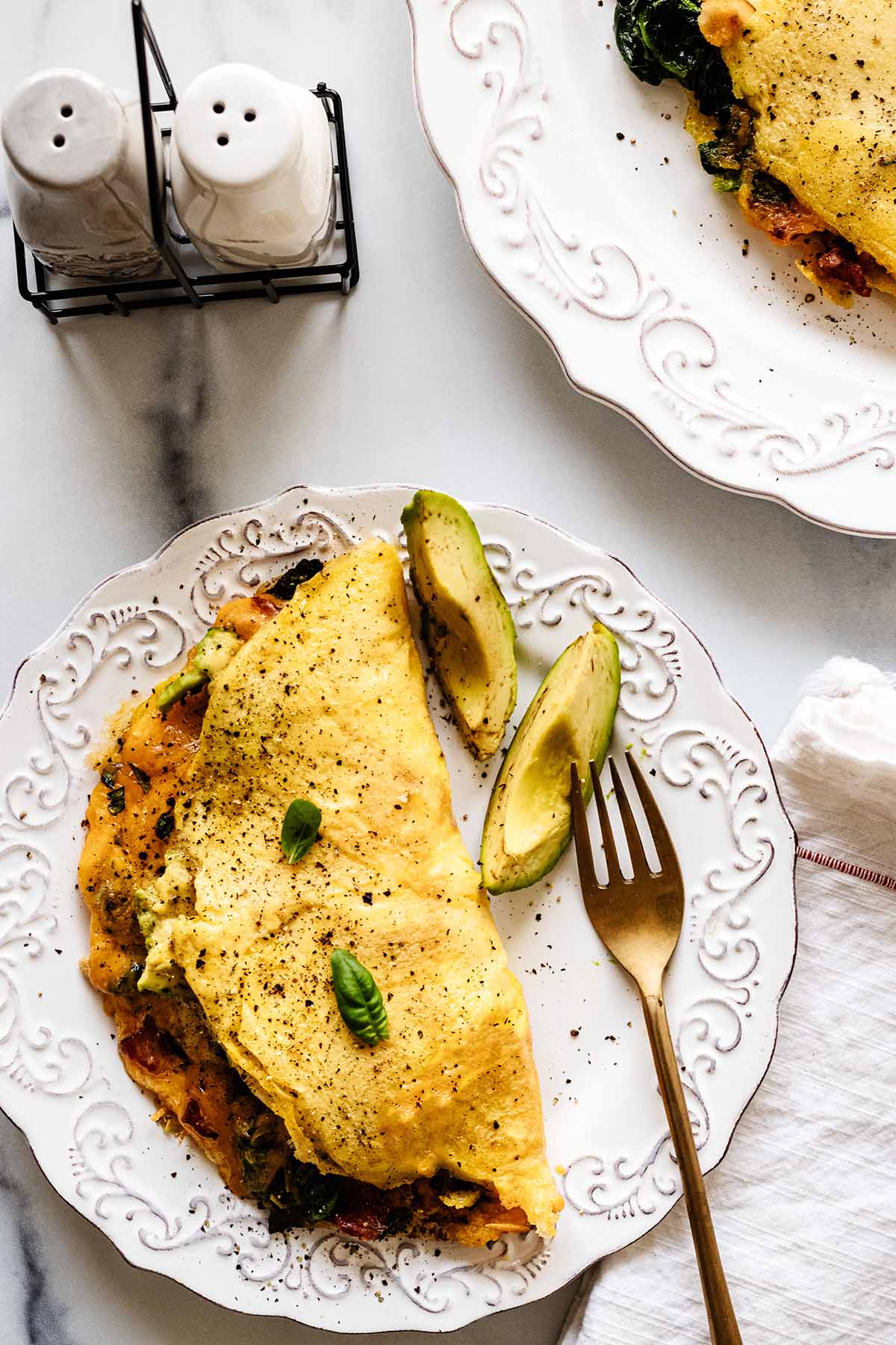 Overhead view of keto omelette on a white plate with pepper and avocado slices and a gold fork