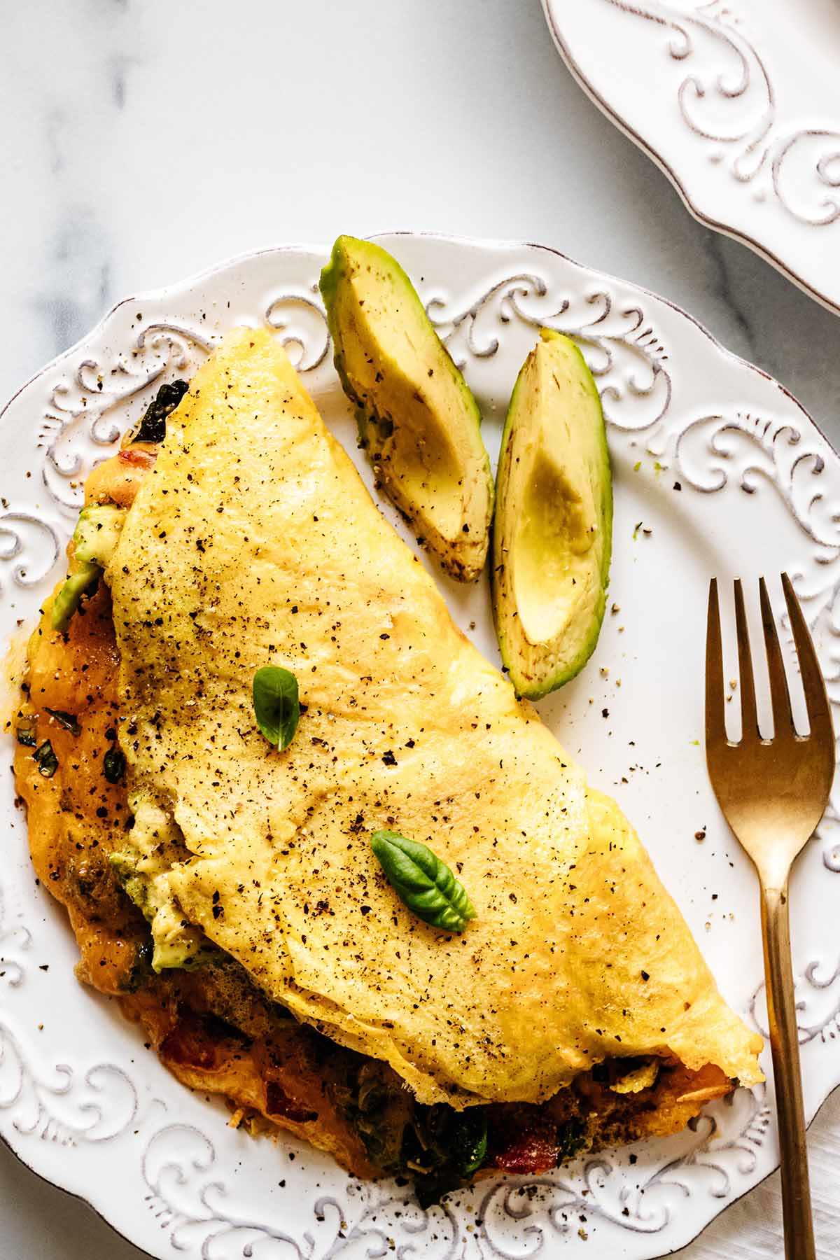 Close up overhead view of keto omelette on a white plate with a gold fork and avocado slices