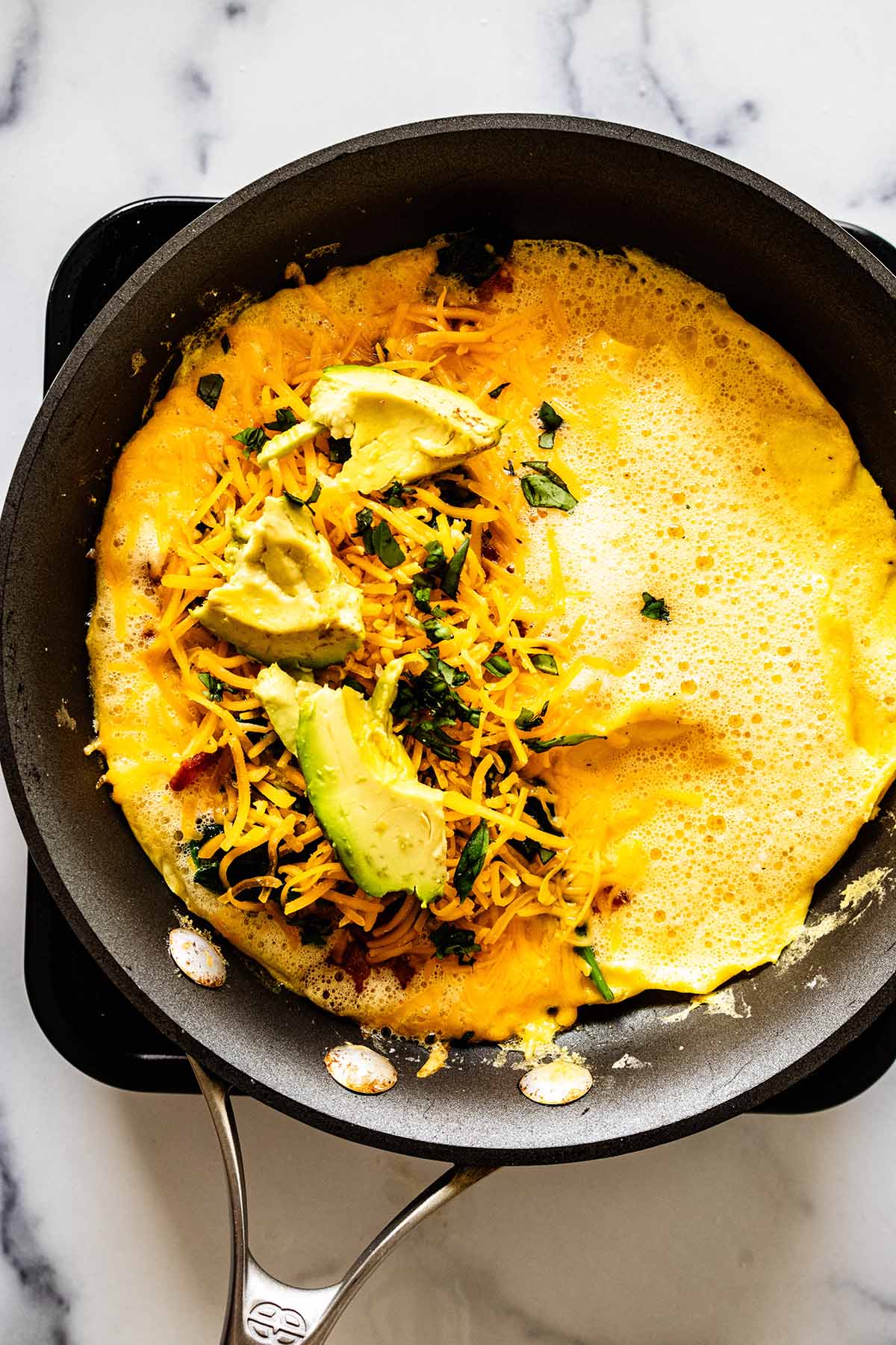 Sliced avocados on top of cheese, spinach and bacon mixture in a skillet