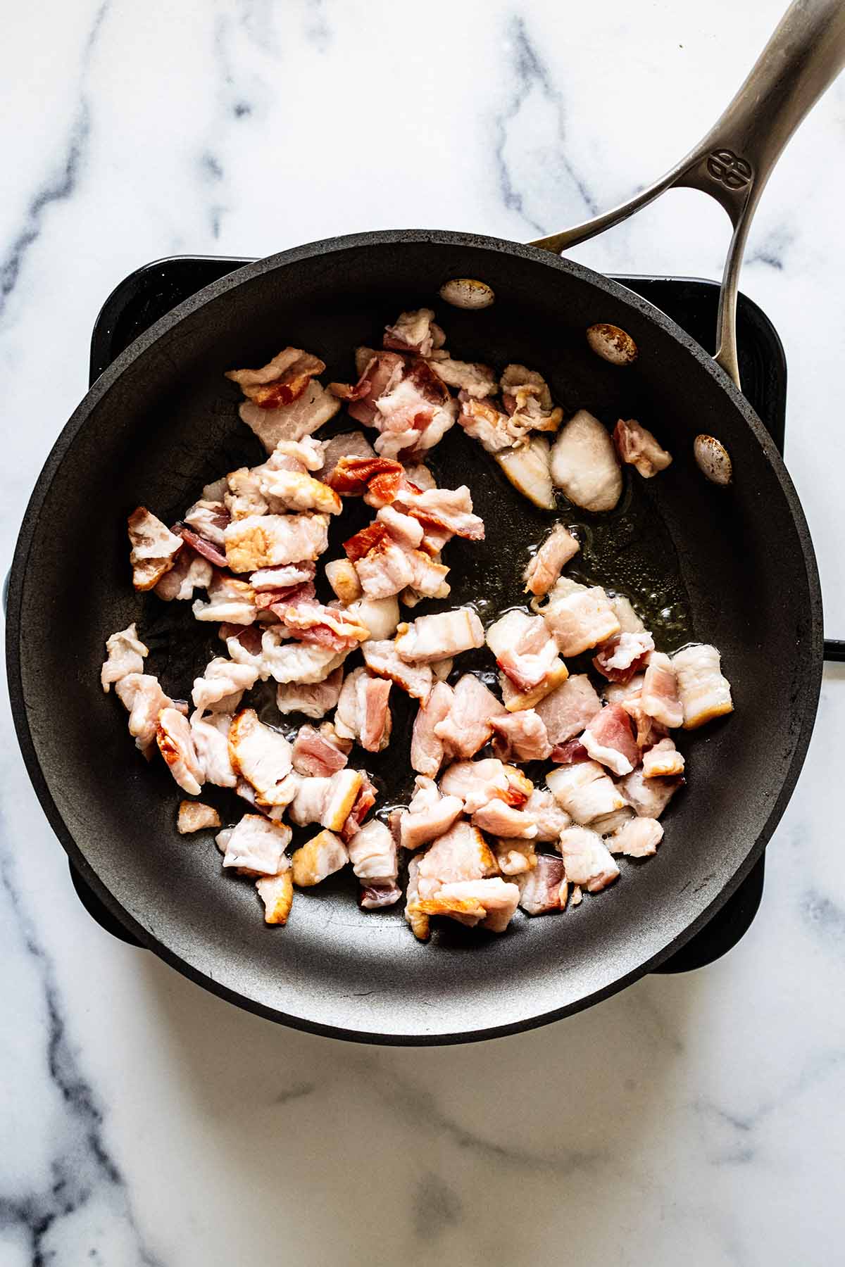 Overhead view of chopped bacon cooking in a skillet