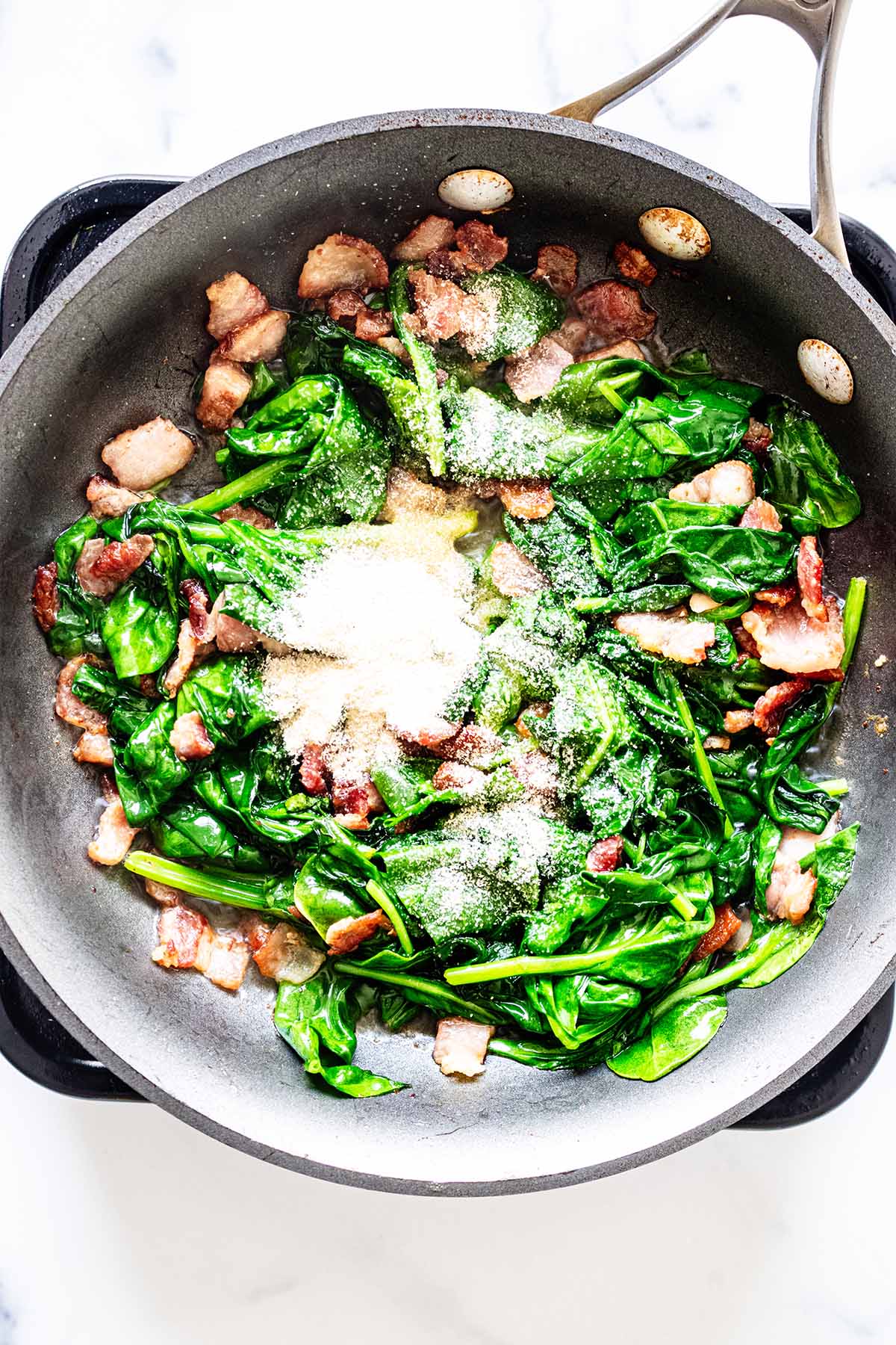 Onion powder, spinach and bacon cooking in a skillet