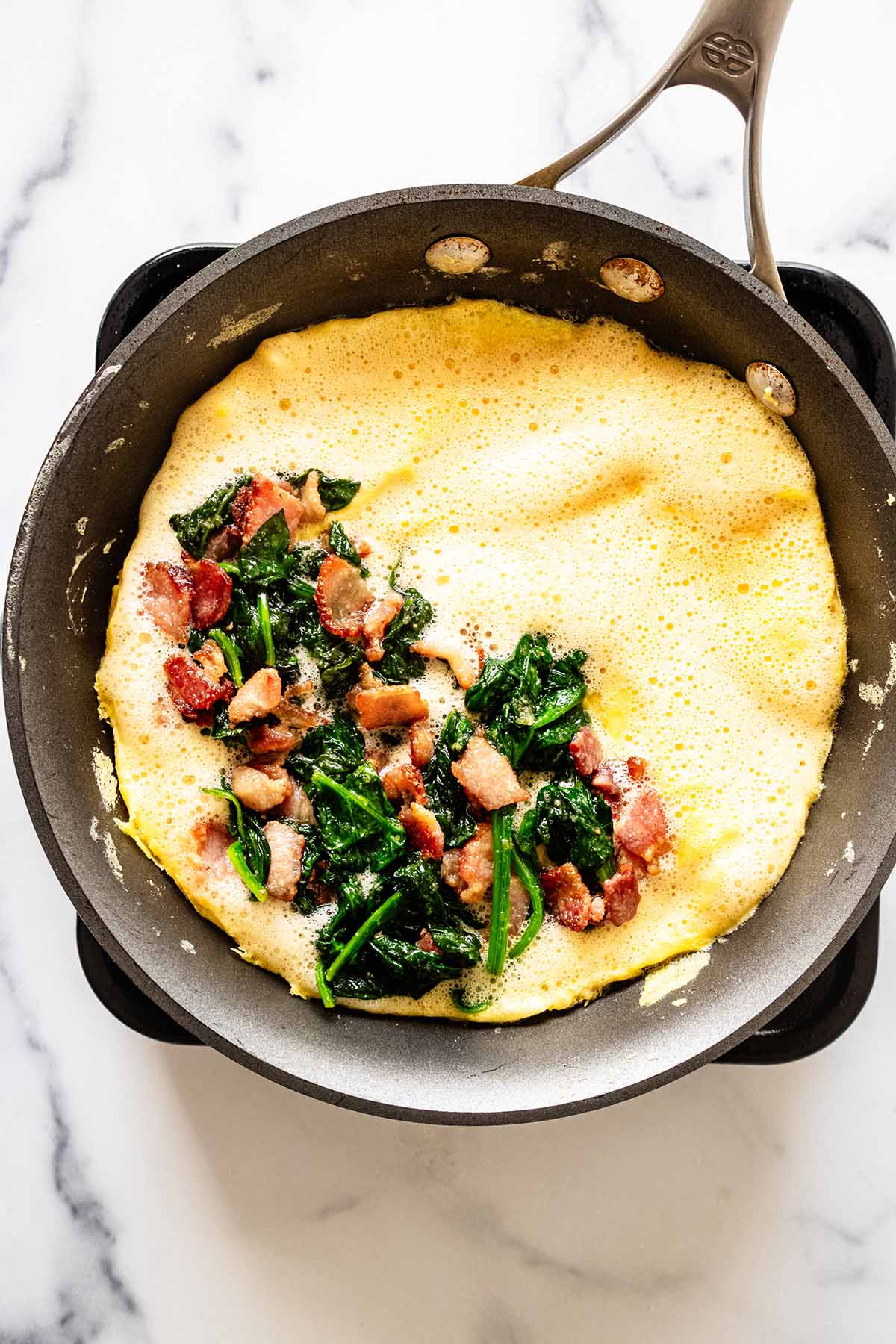 Spinach and bacon mixture on half of the omelette in a skillet