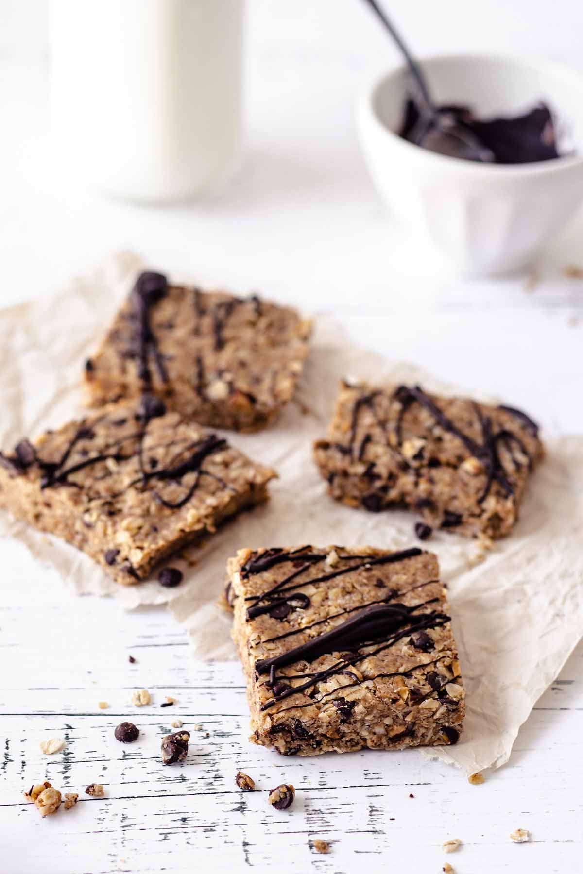 Four no bake oatmeal peanut butter bars on a piece of crumpled paper on a distressed white wood surface
