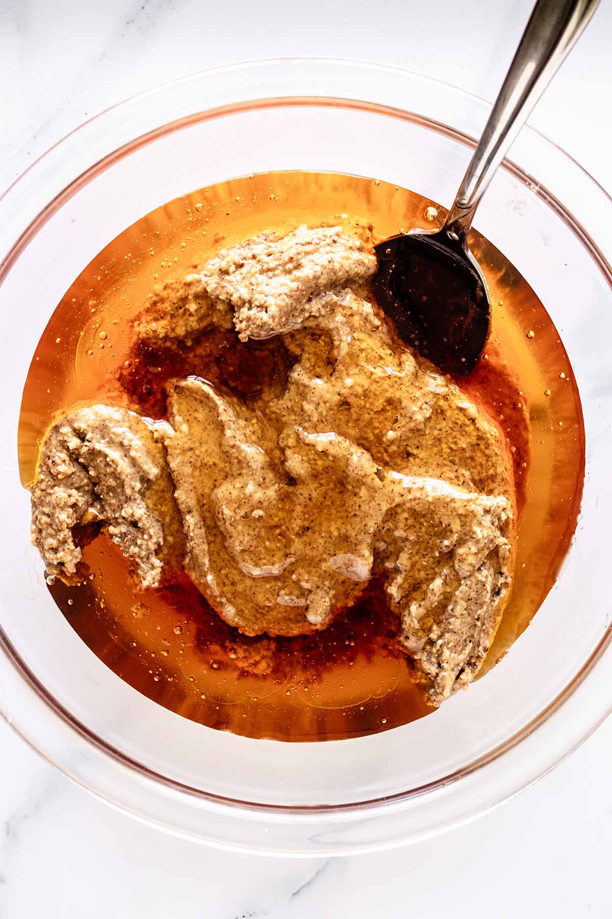 Almond butter, honey and almond extract in a glass bowl with a spoon