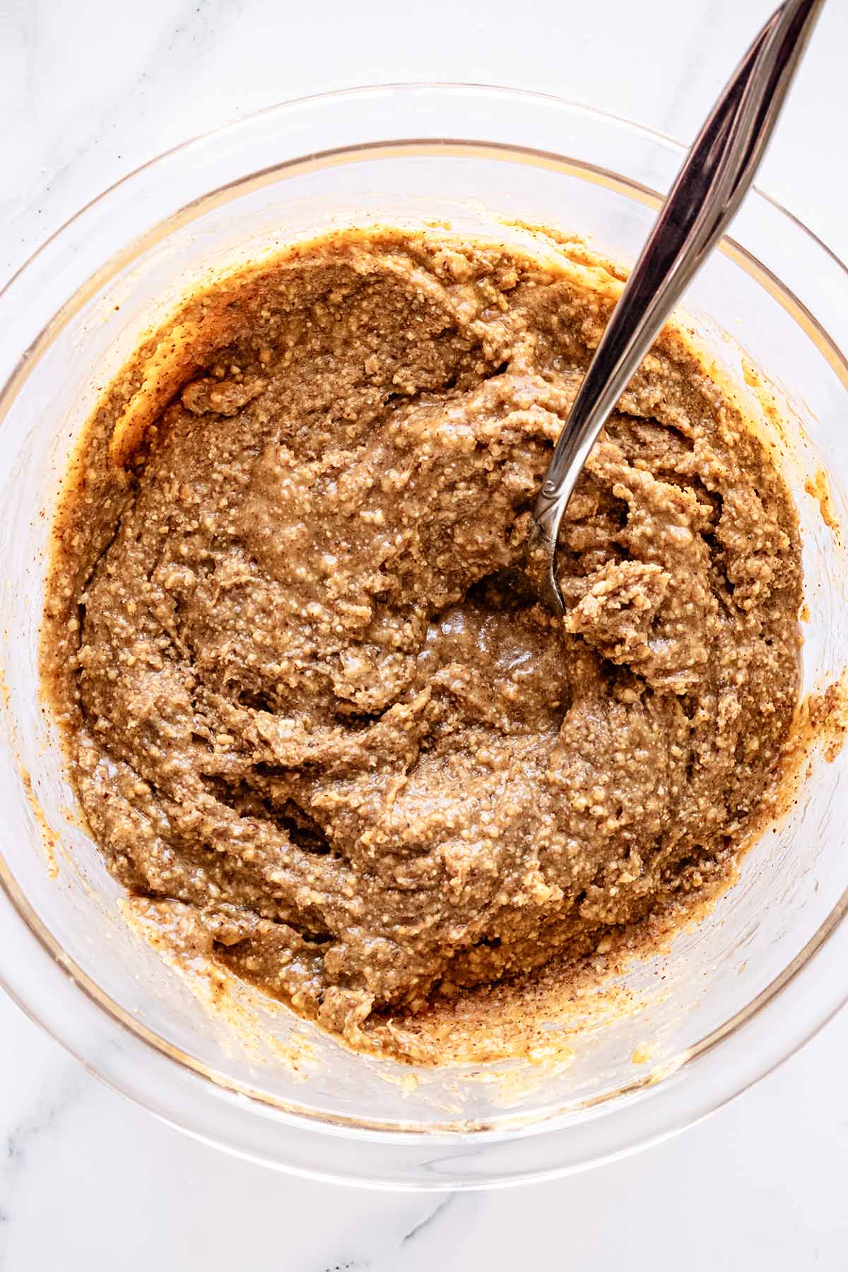 Overhead view of almond butter mixture in a glass bowl with a spoon