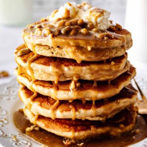 Close up of stack of peanut butter pancakes topped with whipped cream and peanut butter syrup on a white plate
