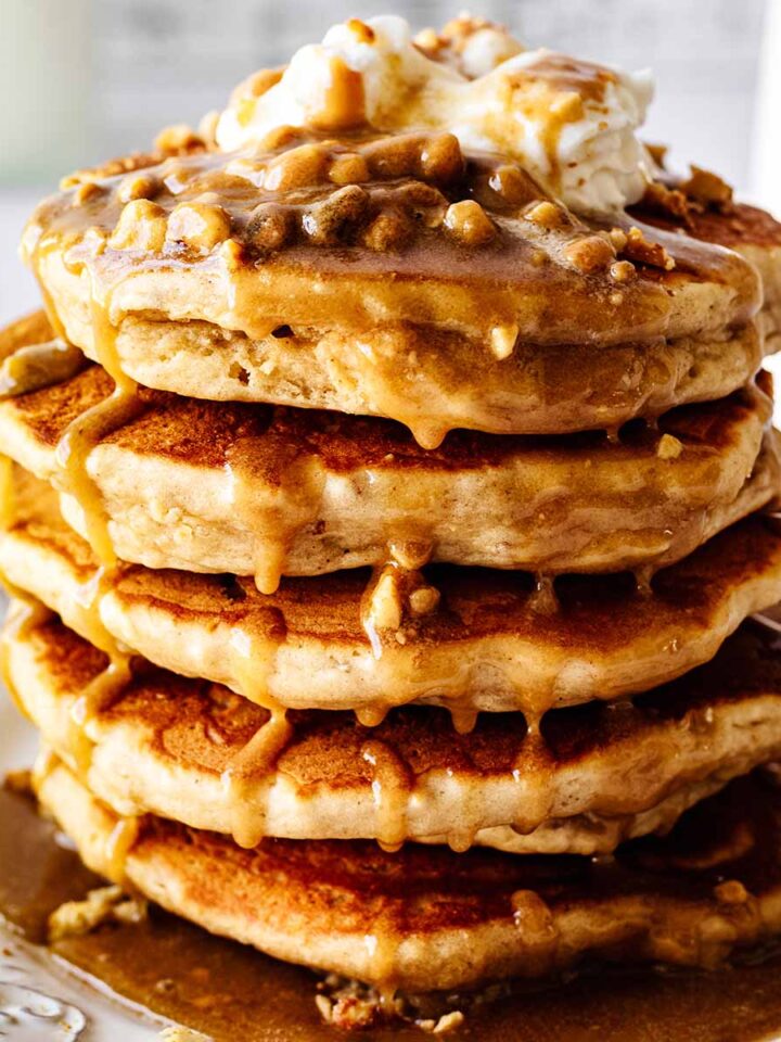 Close up of stack of peanut butter pancakes topped with whipped cream and peanut butter syrup on a white plate