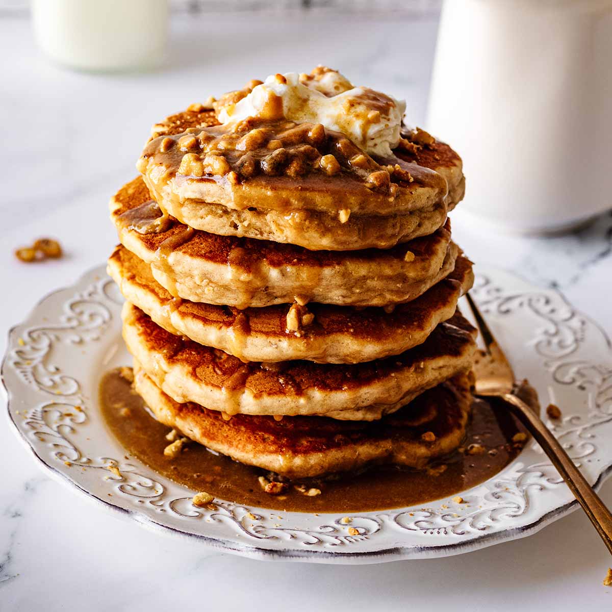 Stack of peanut butter pancakes topped with whipped cream and peanut butter syrup on a white plate