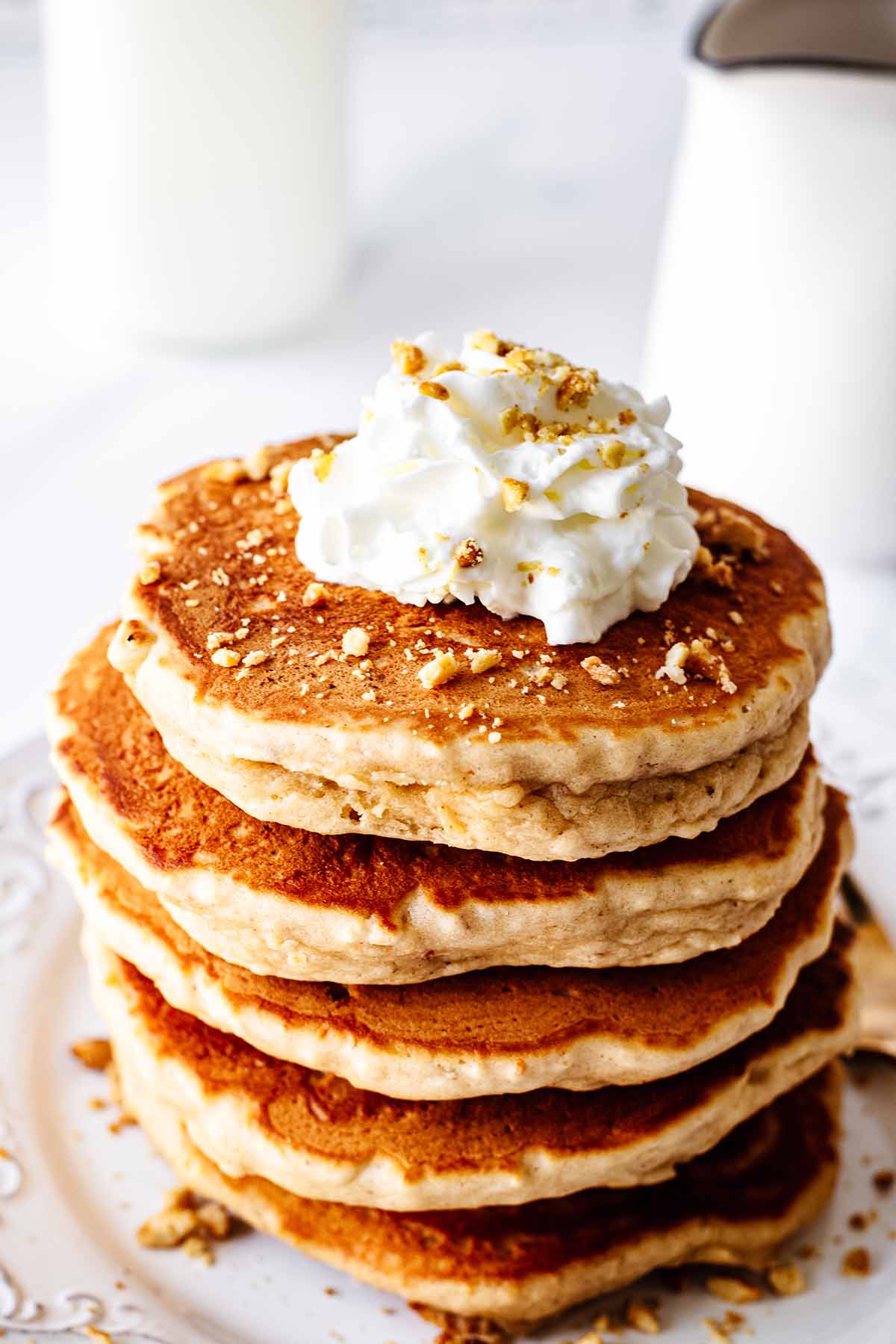 Stack of peanut butter pancakes topped with whipped cream and chopped honey roasted peanuts