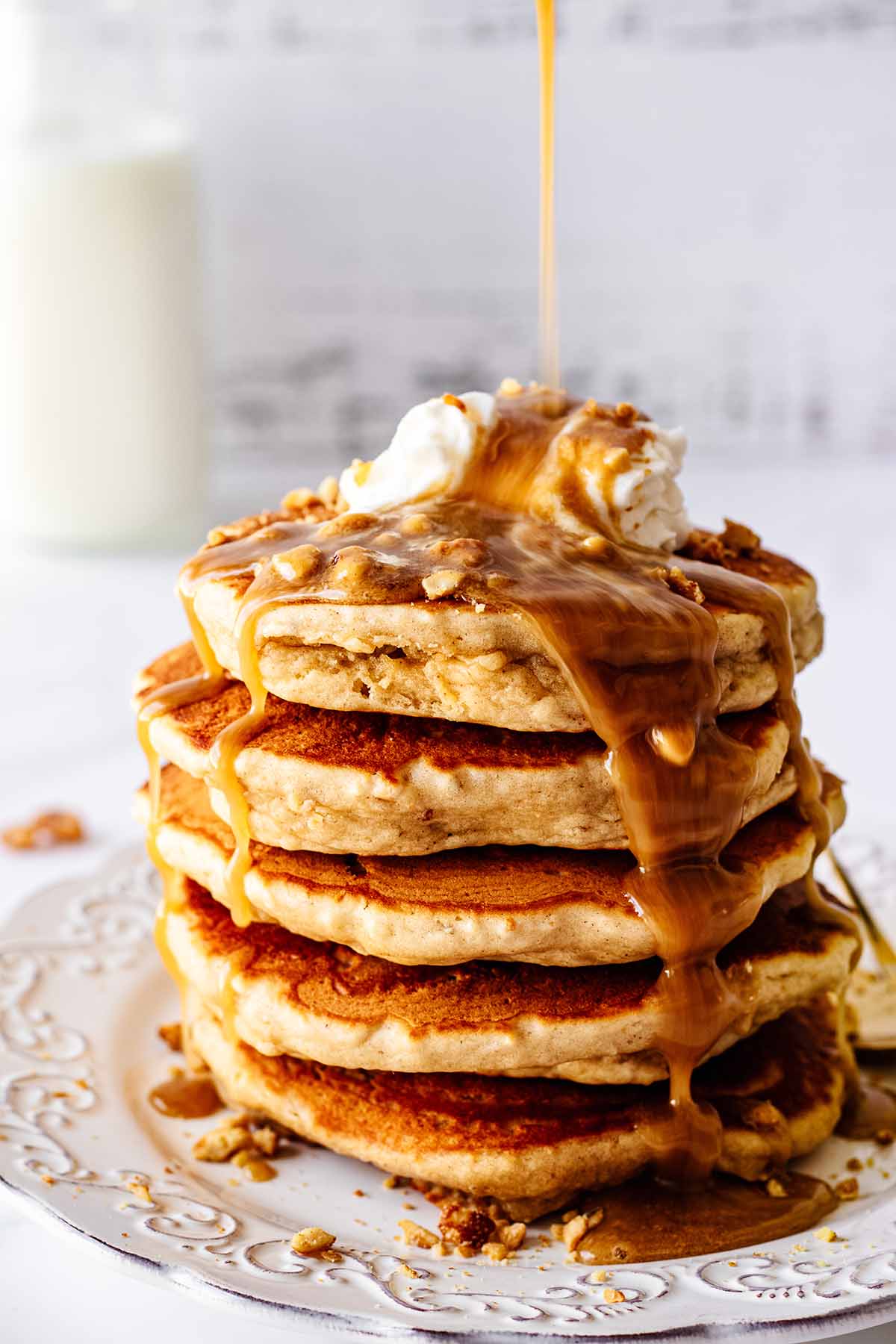 Peanut butter syrup being poured on a stack of peanut butter pancakes on a white plate