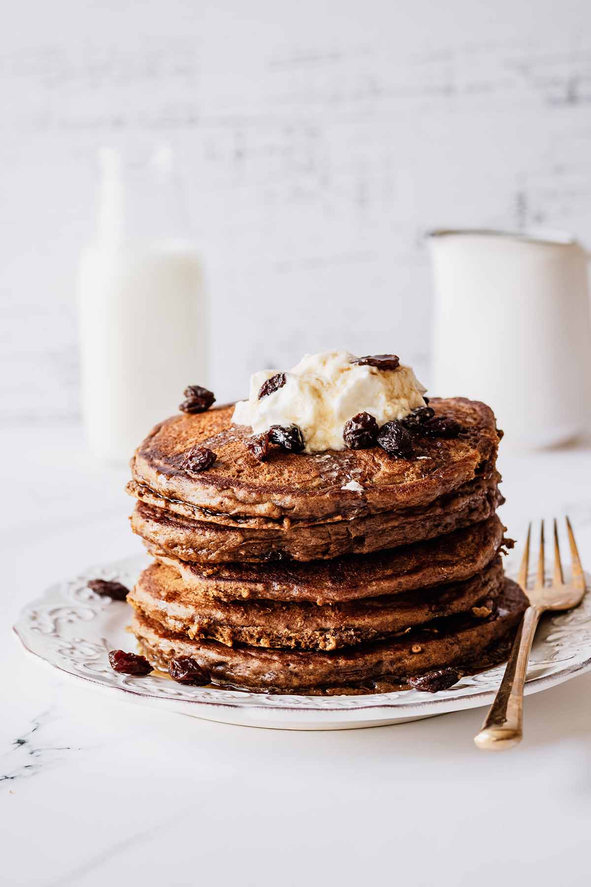 Stack of raisin pancakes topped with whipped cream and raisins on a white plate
