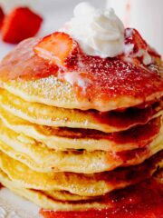 Closeup of a stack of strawberry pancakes topped with whipped cream, strawberry compote and powdered sugar