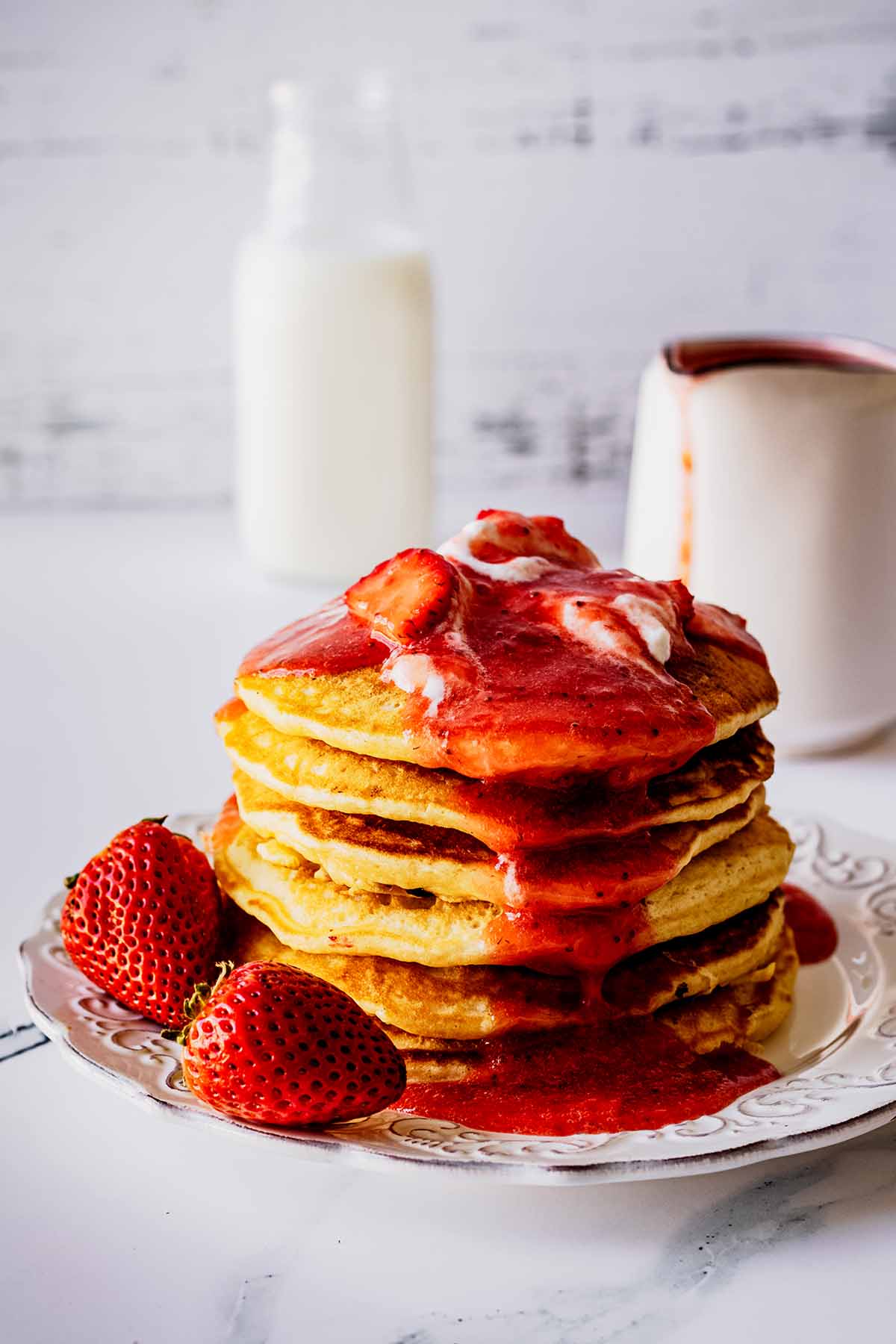 Stack of strawberry pancakes topped with whipped cream and strawberry compote on a white plate