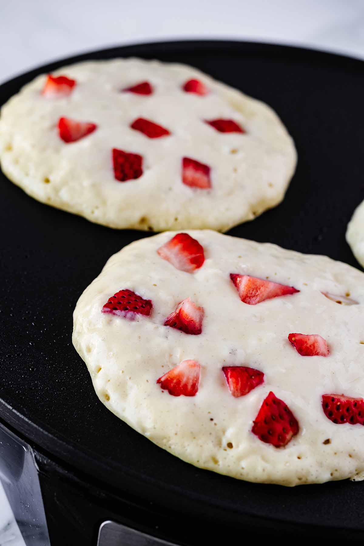 Strawberry pancakes cooking on a griddle