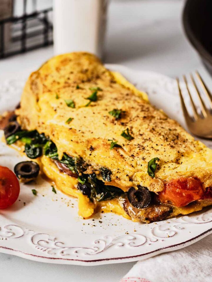 Vegetable omelette on a white plate with tomatoes, basil and a gold fork